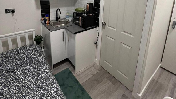 Cocina compacta con lavamanos, hervidor y tostadora. Hay una pequeña encimera y una puerta que da a otra habitación.