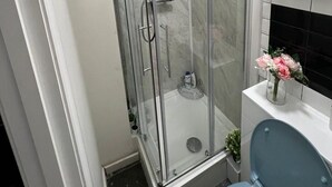 Un baño con ducha de vidrio, inodoro y un florero con flores sobre el lavamanos.