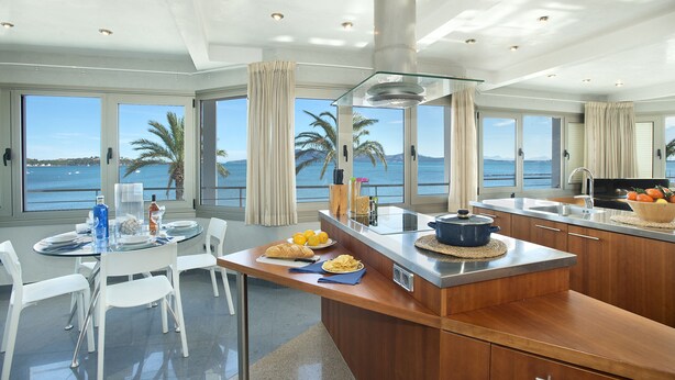 A modern kitchen with a central island, large windows with a sea view, and a dining area with white chairs. - Magnific Apt 2 Sea View by JS Villas (Puerto Pollensa)