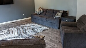 A modern living room with a grey sofa, a patterned rug, and a ceiling fan.