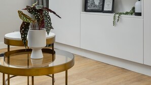 A modern living room with a round glass table, a white cabinet with a mounted TV, and a window with curtains. - Luxurious Studio Apartment | Netflix | Wifi (Cape Town)