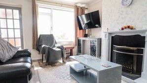 Un salon avec un canapé en cuir noir, un fauteuil gris, une table basse en verre, un téléviseur à écran plat, un meuble et une cheminée.