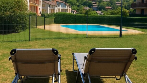 A poolside view with two lounge chairs, a pool, and a backdrop of residential buildings and hills.