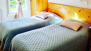 A room with two beds, wooden headboards, a window with curtains, and a wall-mounted light fixture.