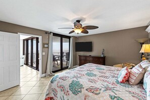 Un dormitorio con cama, ventilador de techo, televisión y puerta corrediza de vidrio que da a un área exterior.