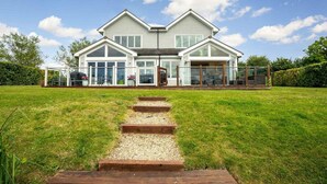 A two-story house with a large front lawn, a wooden staircase leading to the front door, and a covered patio area.