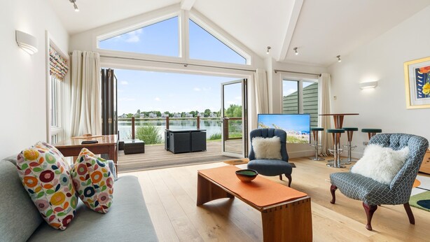 A spacious living room with a large window, a sofa with colorful cushions, a wooden coffee table, a blue armchair, and a TV.