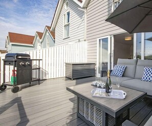 A deck with a grill, a table with a bottle and glasses, and a sofa with cushions.