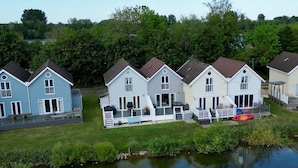 A row of houses with attached porches, a small dock, and a calm water body in the foreground. - Spring Lake 14, Lakeside Retreat - Waterside Lodge, Watersports, Sleeps 6 (South Cerney)