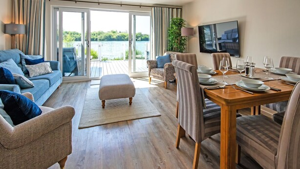 A modern living room with a dining area, large windows, and a view of a body of water. - Spring Lake 14, Lakeside Retreat - Waterside Lodge, Watersports, Sleeps 6 (South Cerney)