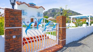 Una villa bianca con tetto in tegole, piscina e montagne sullo sfondo.