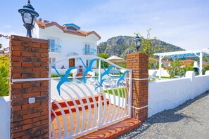Une villa blanche avec un toit en tuiles, une piscine et une vue sur les montagnes en arrière-plan.