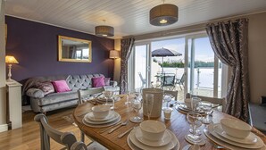 Ein Essbereich mit einem Holztisch, gedeckt für sechs Personen, einem grauen Sofa mit rosa Kissen und einem großen Fenster mit Vorhängen.