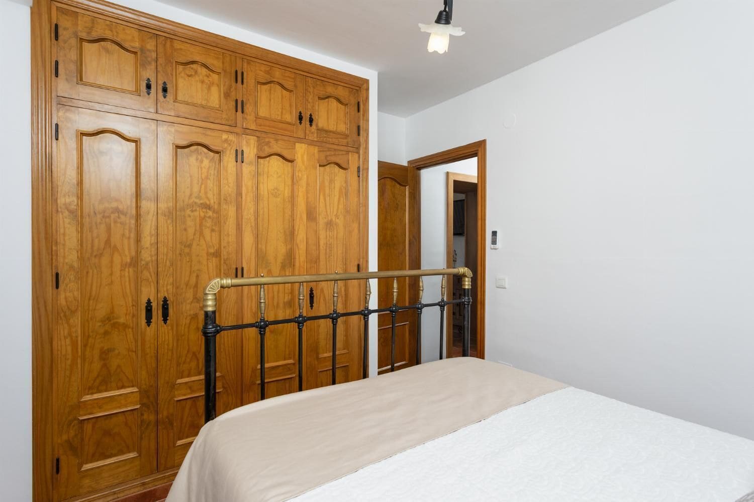 A bedroom with a large wooden wardrobe, a bed with a metal headboard, and a white wall.