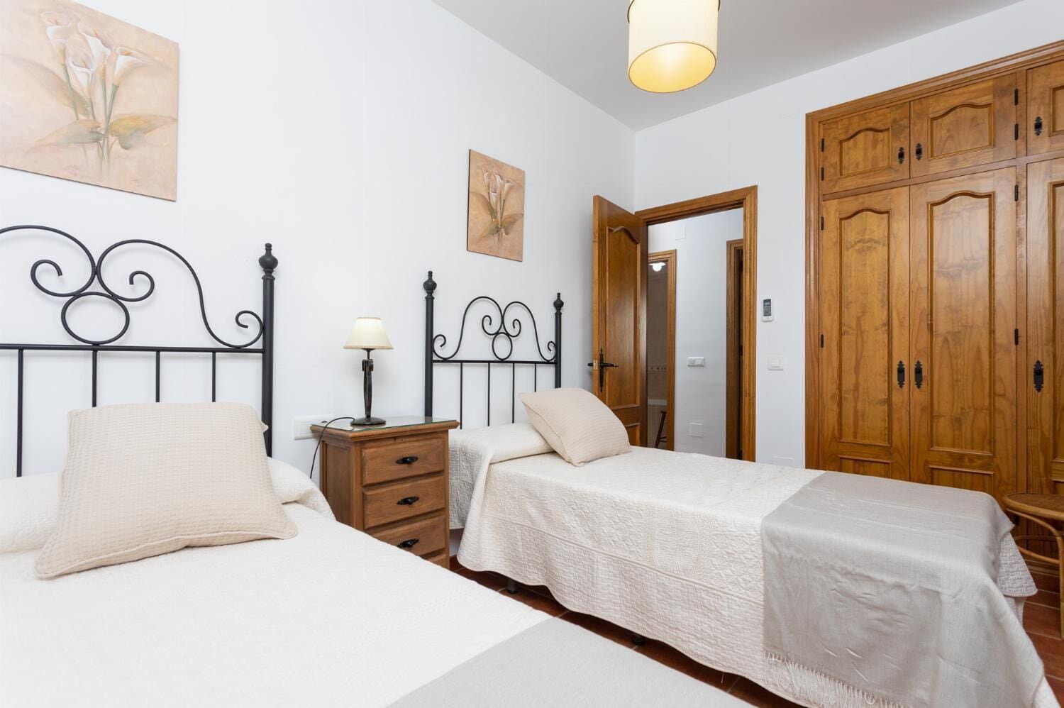 A bedroom with two beds, a nightstand, a lamp, and wooden wardrobes.
