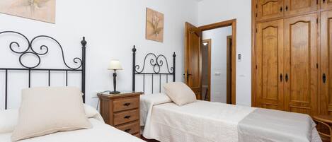 A bedroom with two beds, a nightstand, a lamp, and wooden wardrobes.