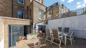 An outdoor patio with a table and chairs, a potted plant, and a cat house. - Fabulous Fulham - Two Bedroom Apartment, Sleeps 4 (London)