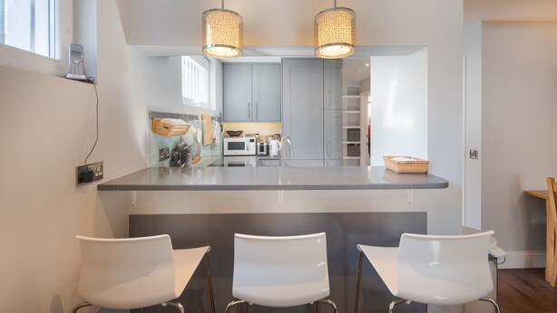 A modern kitchen with a central island, two pendant lights, and a breakfast bar with three white chairs. - Fabulous Fulham - Two Bedroom Apartment, Sleeps 4 (London)