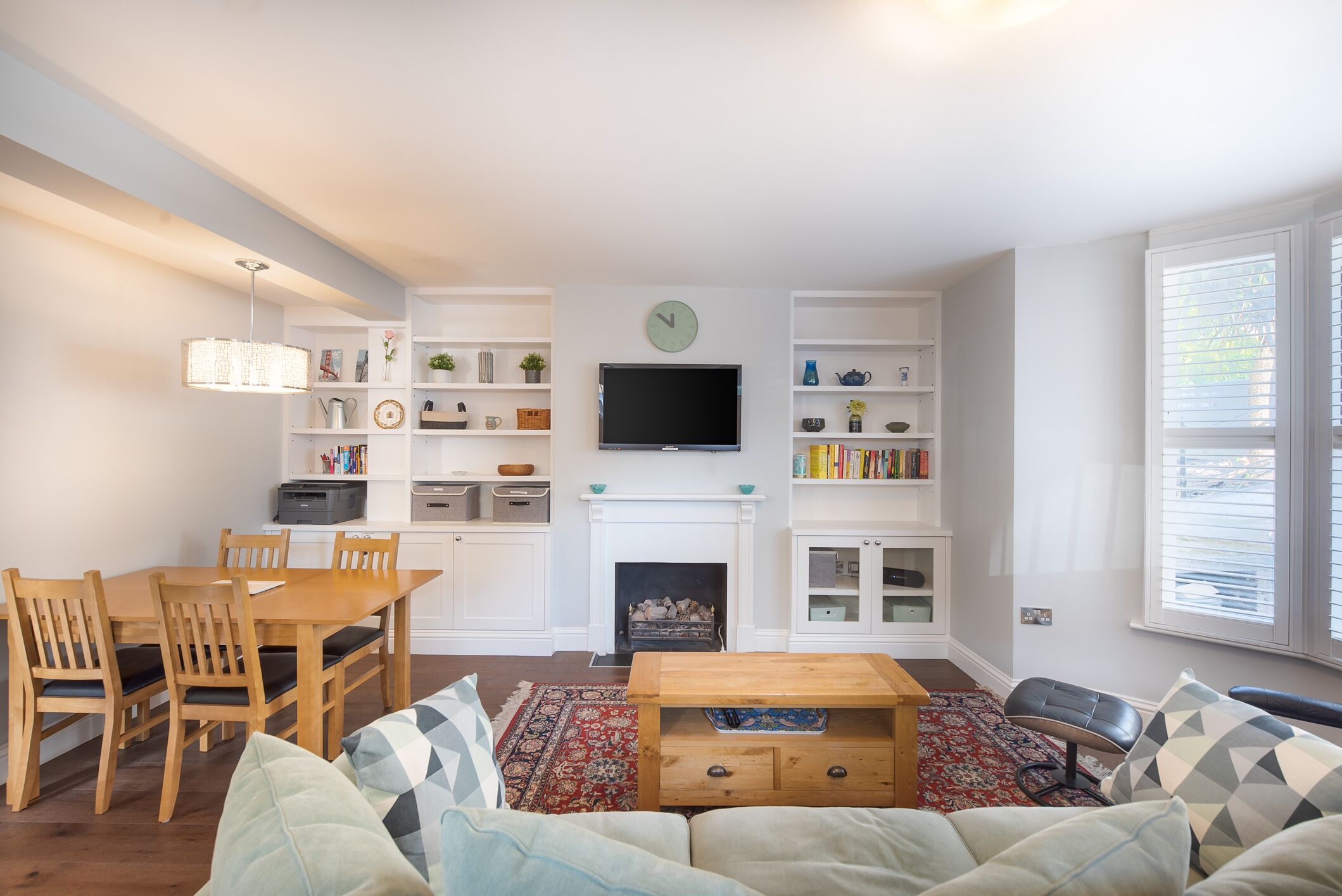 A modern living room with a dining area, a fireplace, and a TV mounted above it.