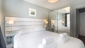 A modern hotel room with a large bed, bedside lamps, a bedside table, a mirror, and a framed picture on the wall. - Fabulous Fulham - Two Bedroom Apartment, Sleeps 4 (London)
