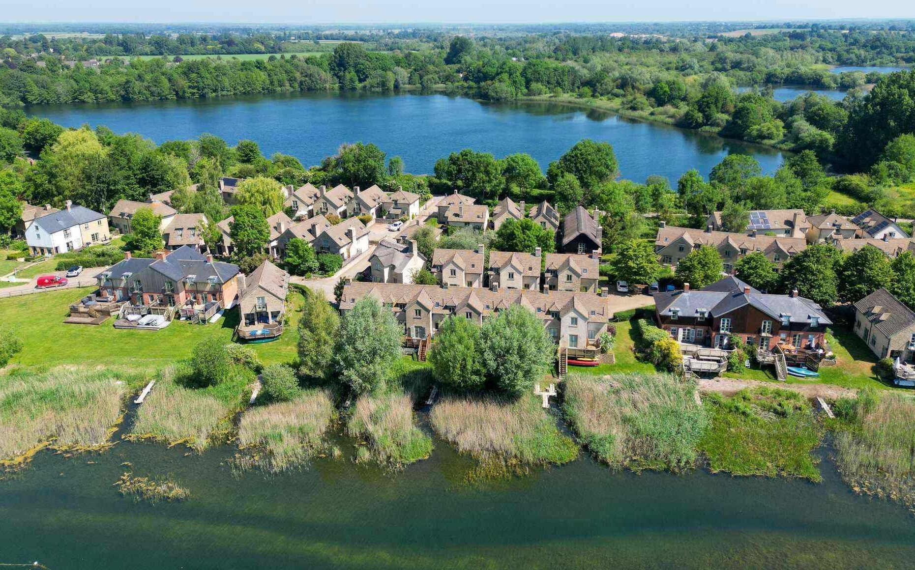 An aerial view of a residential area with houses clustered around a lake, surrounded by greenery.