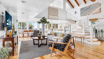 A spacious living area with a staircase, wooden flooring, and a large window offering a view of the outdoors.
