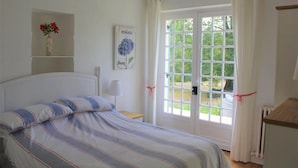 Un dormitorio con una cama, una ventana con cortinas, una mesita de noche, una lámpara y un estante en la pared con un jarrón.