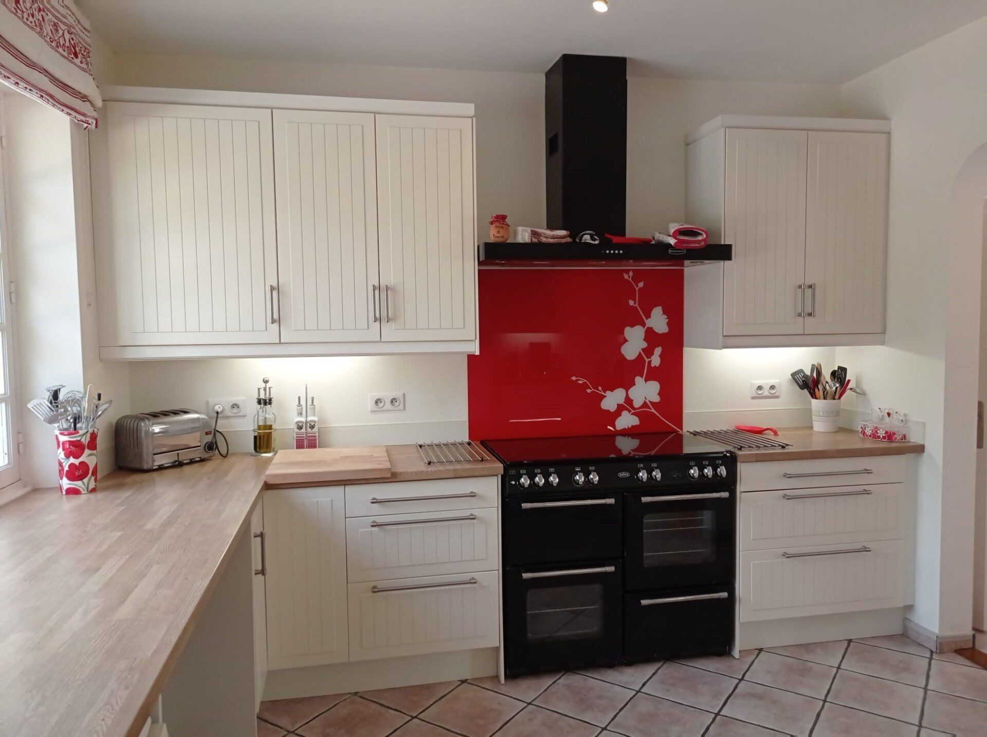 Una cocina con armarios blancos, un electrodoméstico rojo y una encimera de madera.