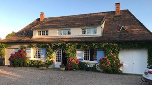 Una casa de dos plantas con un camino de grava y un coche aparcado.