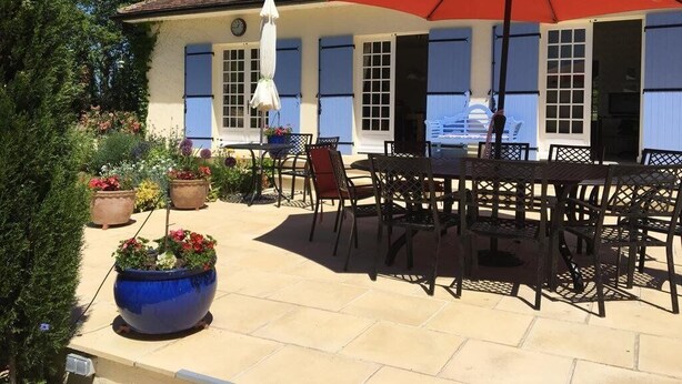 Un patio con una mesa, sillas, un paraguas rojo y plantas en macetas.