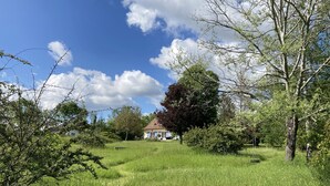 Una casa rodeada de campos verdes y árboles bajo un cielo azul despejado.