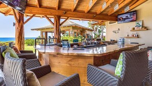 Un coin bar en bois, avec des meubles en osier, un téléviseur et une vue sur l’océan.