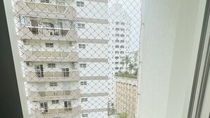 Un petit balcó amb una tanca de malla metàl·lica, un paviment de rajoles i vista a edificis alts.