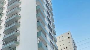 Un edifici residencial de diverses plantes amb balcons, una zona d'aparcament i vista al carrer.