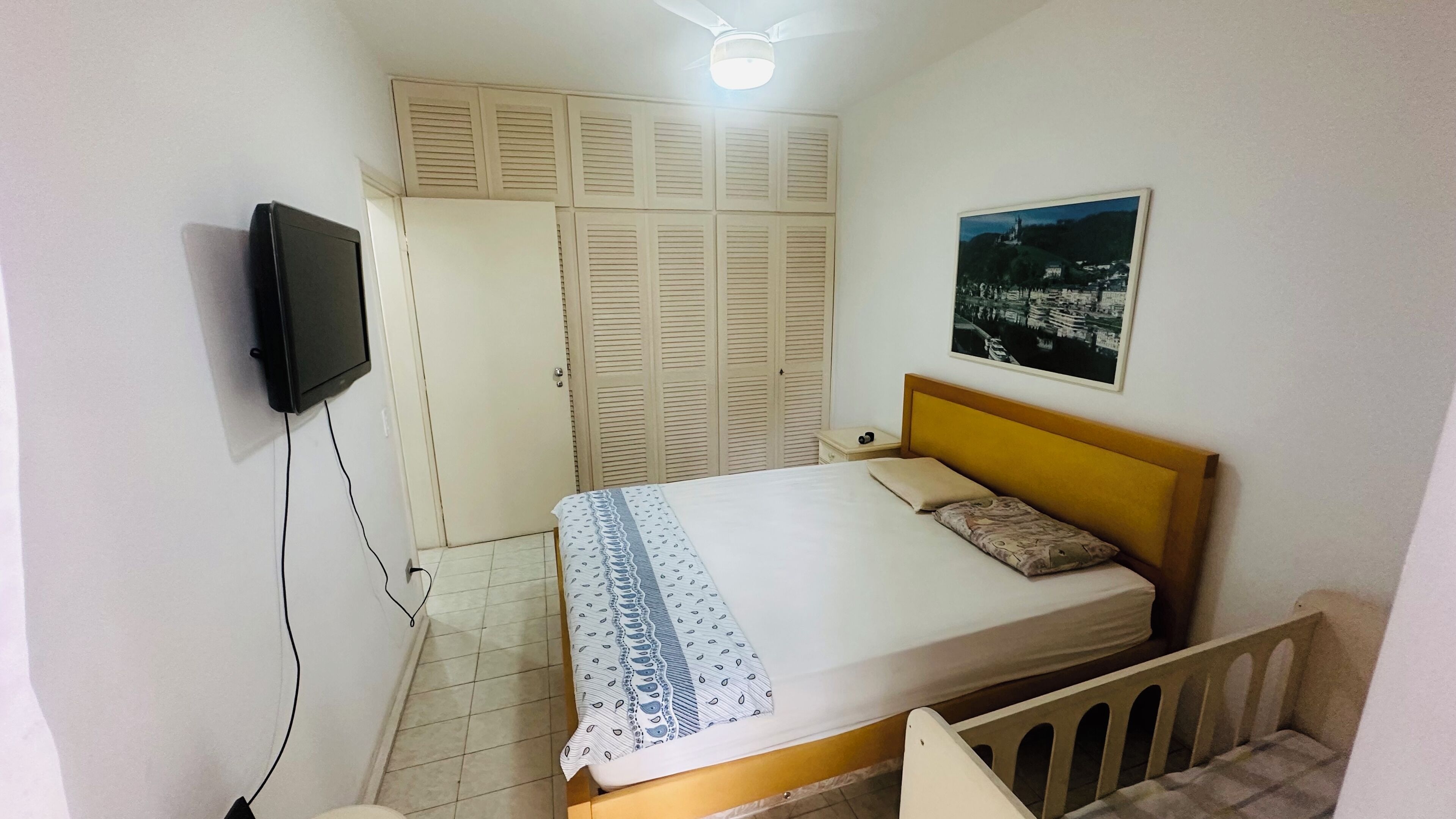 Un dormitorio con cama, televisor montado en la pared, armario y ventilador de techo.