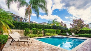 A rectangular swimming pool with a tiled edge, surrounded by a brick patio. There are lounge chairs and a small hot tub area. - Encore Resort 11 Bedroom Home with Pool (2206) (Kissimmee)