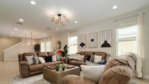 A spacious living room with two brown leather sofas, a coffee table, and a chandelier. - Encore Resort 11 Bedroom Home with Pool (2206) (Kissimmee)