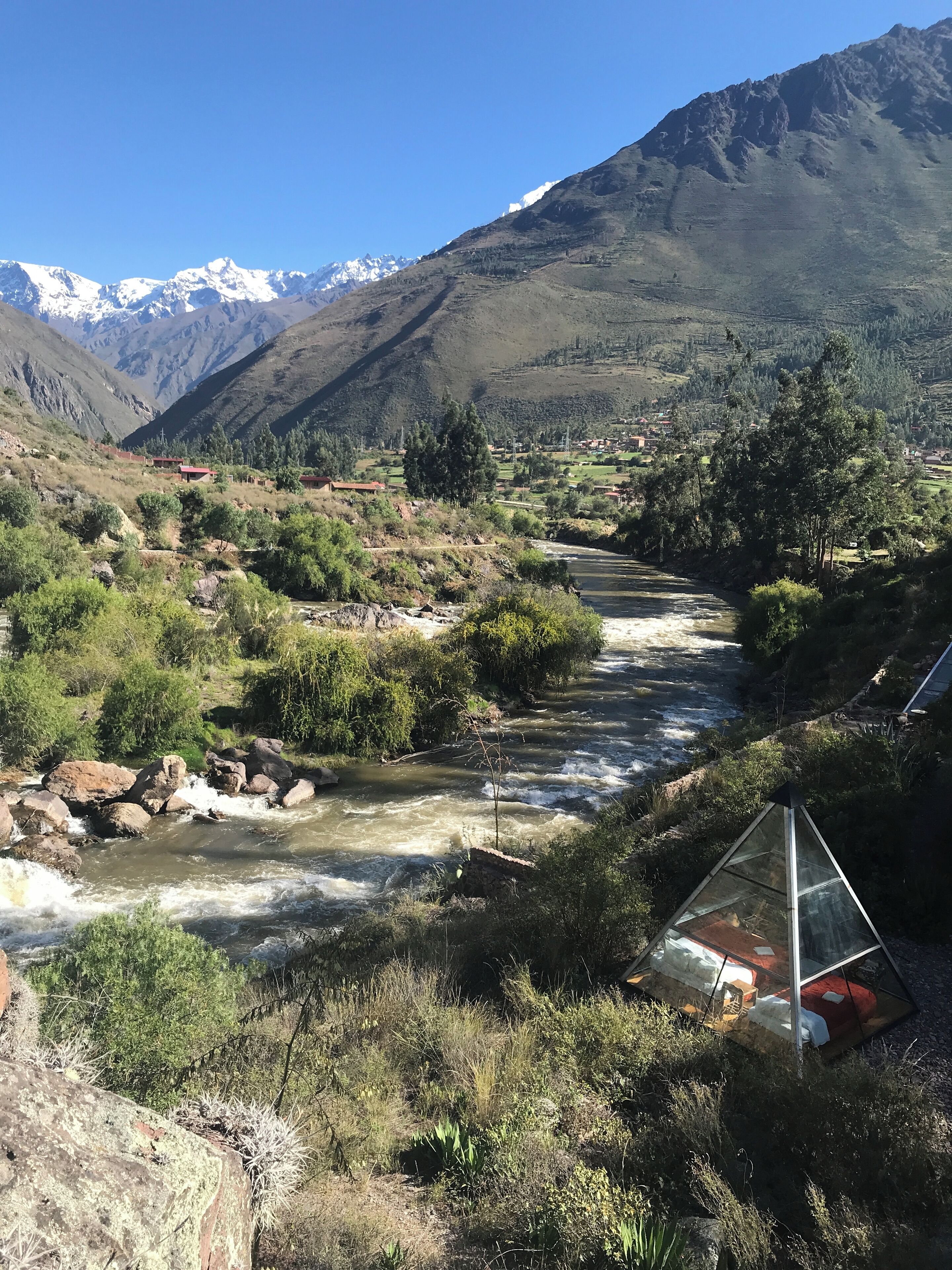 Een rivier die door een bergachtig landschap stroomt, met een kleine kasachtige constructie in de buurt van het water.