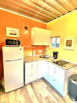 A compact kitchen with white cabinets, a microwave, a sink, and a coffee maker.