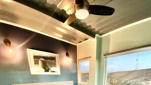 Een slaapkamer met een bed, nachtkastje en een raam met uitzicht op een strand.