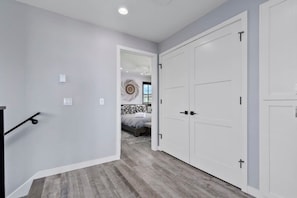 Un couloir avec un plancher en bois, des murs blancs et un lit à l’arrière-plan.