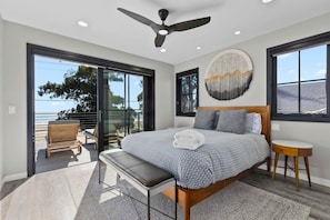 Une chambre dotée d’un grand lit, d’un ventilateur de plafond, d’une vue sur l’océan et d’un balcon avec des sièges d’extérieur.