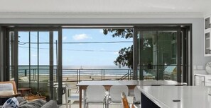 A modern kitchen with a large sliding glass door leading to a balcony overlooking a beach.