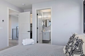 A bedroom with a bed, a bathroom with a mirror, and a hallway leading to a staircase.
