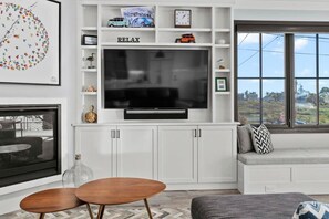 A living room with a flat-screen TV, white cabinetry, a seating area with a sofa, and a window with a view. - Luxury Twin Lakes Beachhouse (Santa Cruz)