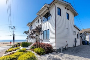 Een wit huis met twee verdiepingen, een overdekte veranda, een kleine tuin en uitzicht op het strand.