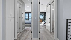 Un pasillo moderno con puertas blancas, una cama al fondo y vistas al exterior.