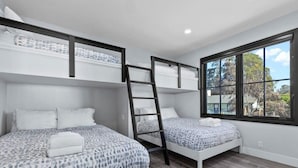 Una habitación con dos literas, una escalera y una ventana que da a árboles.