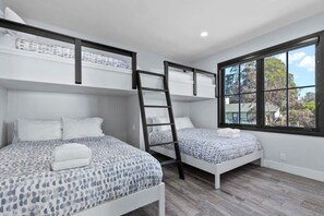 Une chambre avec deux lits superposés, une échelle et une fenêtre donnant sur les arbres.