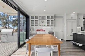 Une cuisine moderne avec des meubles blancs, une table à manger en bois et une vue sur l’extérieur.